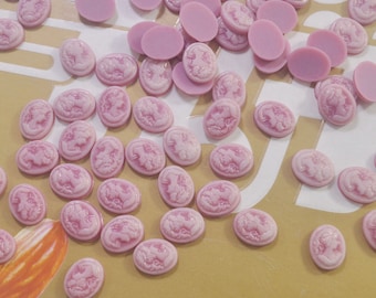 May include: A collection of pink oval-shaped cameo-style resin cabochons with raised white designs. The cabochons are scattered on a light brown surface.