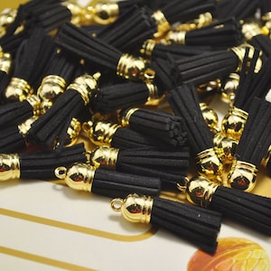 May include: A pile of black tassel charms with gold metal caps. The tassels are made of soft, fuzzy material and are about 1 inch long.
