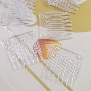 May include: A set of five clear plastic hair combs. The combs are small and rectangular with a row of teeth on one side.