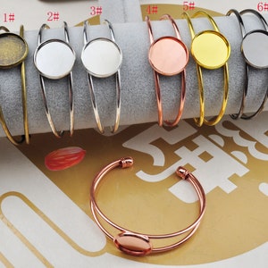 May include: Six different styles of metal bangle bracelets with a round, clear glass cabochon. The bracelets are numbered 1 through 6. The cabochons are in different colours, including silver, gold, copper, and black.