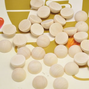 Puede incluir: Una colección de suministros de artesanía de madera redonda y blanca. Las piezas de madera son lisas y tienen un acabado ligeramente brillante.