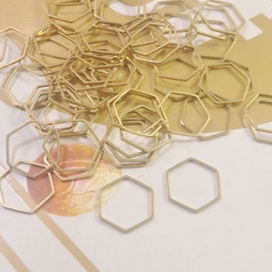 May include: A large quantity of gold-coloured metal hexagonal jump rings. The rings are scattered on a light brown surface.