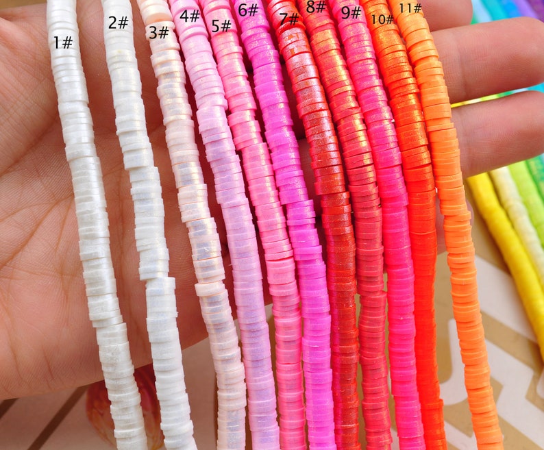 Pu&ograve; includere: Assortimento di 11 fili di perline di plastica iridescente colorate. Le perline sono piccole e rotonde, e sono disposte in fila dal bianco all'arancione. Le perline sono tutte della stessa dimensione e forma, e sono infilate su uno spago trasparente.