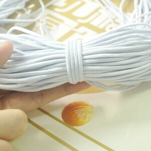 May include: A close-up of a bundle of white elastic cord. The cord is soft and flexible, and it is ideal for crafting projects.