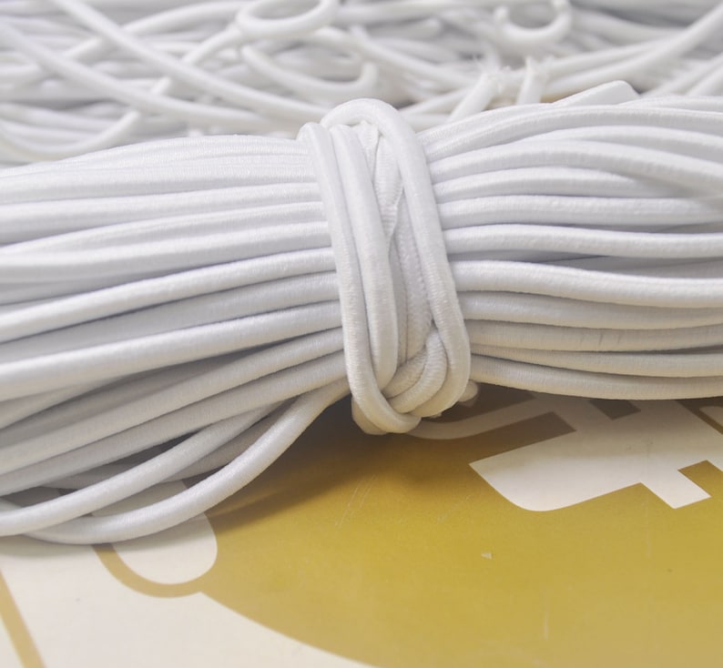 May include: A close-up of a large spool of white elastic cord. The cord is tightly wound and appears to be made of a soft, stretchy material.