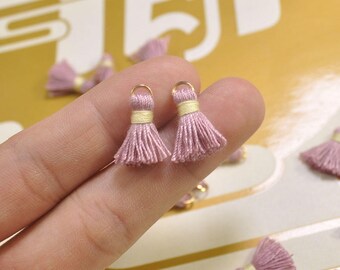 May include: Two pink tassel charms with gold rings. The tassels are made of soft yarn and have a subtle sheen.