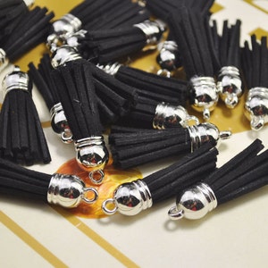 Peut inclure: Un groupe de breloques en forme de pompon noir avec des embouts et des boucles en métal argenté. Les pompons sont faits d'un matériau doux et moelleux et sont parfaits pour ajouter une touche d'élégance à tout projet.