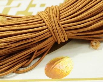 May include: A close-up of a spool of brown elastic cord. The cord is tightly wound and has a smooth, matte finish.