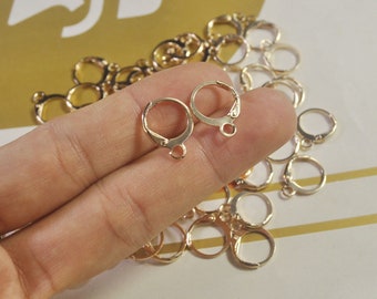May include: A close-up of a pile of gold-colored earring hooks. The hooks are made of metal and have a simple, circular design.