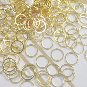 May include: A large pile of gold jump rings, a type of jewelry finding, scattered on a white surface.