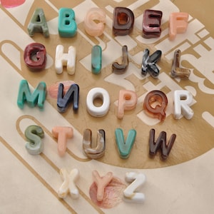 May include: A collection of colorful, translucent alphabet letters in various shades of green, blue, brown, pink, and white. The letters are arranged in rows and columns, showcasing the full alphabet from A to Z. The letters have a glossy finish.