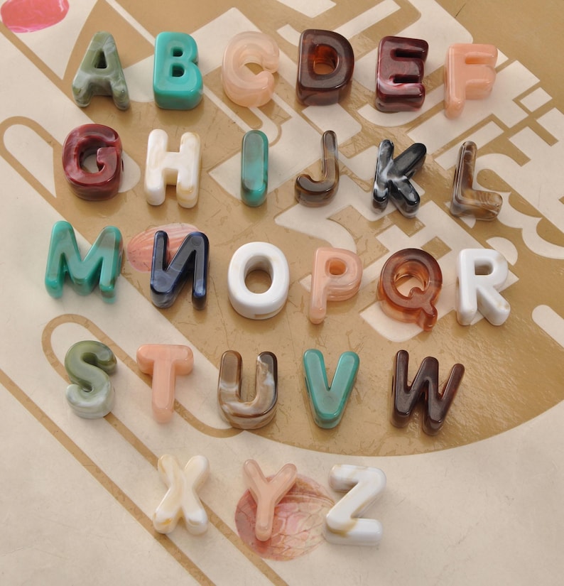 May include: A collection of colorful, translucent alphabet letters in various shades of green, blue, brown, pink, and white. The letters are arranged in rows and columns, showcasing the full alphabet from A to Z. The letters have a glossy finish.