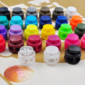 May include: Assortment of colorful plastic toggle clasps in various colors, including red, blue, green, yellow, purple, and black. The clasps are arranged in rows on a brown surface.