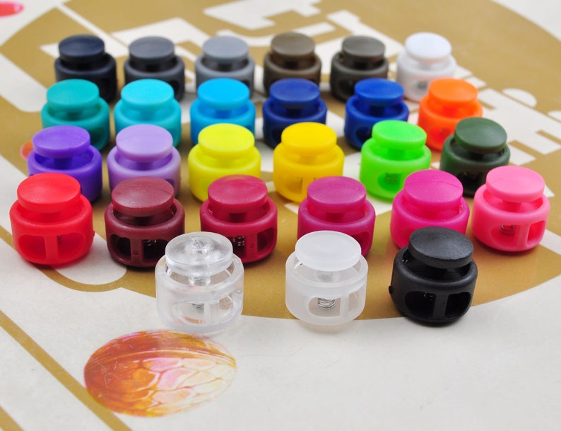 May include: Assortment of colorful plastic toggle clasps in various colors, including red, blue, green, yellow, purple, and black. The clasps are arranged in rows on a brown surface.