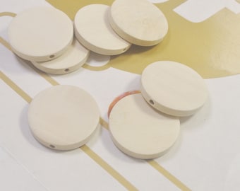 May include: A group of six off-white round wooden discs with a hole in the center. The discs are arranged in a random pattern on a white surface.
