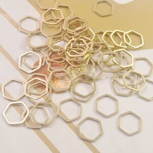 May include: A large pile of gold-coloured metal hexagonal jump rings. The rings are all the same size and are arranged in a random pattern.