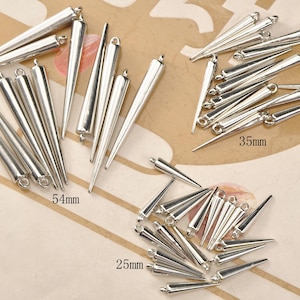 May include: A collection of silver-coloured metal cone-shaped charms, perfect for jewellery making. The charms have loops and come in various sizes, including 25mm, 35mm, and 54mm long. Ideal for earrings, pendants, and other accessories.