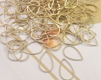 May include: A large pile of gold-colored metal teardrop-shaped earring blanks. The blanks are arranged in a random pattern and are scattered on a white surface.