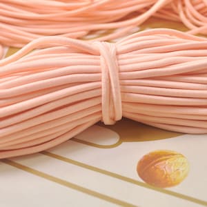 May include: A close-up of a large spool of peach-coloured elastic cord. The cord is tightly wound and appears to be soft and stretchy.