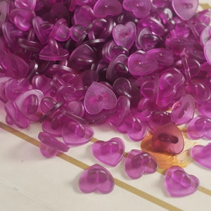 May include: A large pile of purple heart-shaped plastic buttons with a small pin on the back.