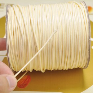 May include: A spool of off-white waxed cord, wound tightly and ready for use in crafting projects.