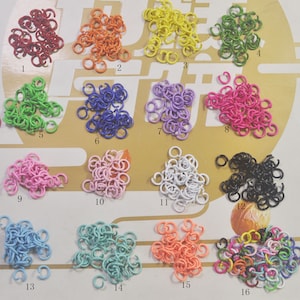 May include: Assortment of 16 different coloured metal jump rings. The rings are arranged in rows of two, with each row numbered 1 through 16. The rings are all the same size and shape, but they are different colours, including red, orange, yellow, green, blue, purple, pink, white, black, light blue, light green, light orange, and multi-coloured.