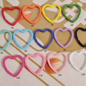 May include: Thirteen heart-shaped metal keyrings in various colours, including red, yellow, green, blue, turquoise, pink, and white. Each keyring is numbered 1 through 13.
