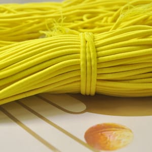 May include: A close-up of a bundle of bright yellow elastic cord. The cord is tightly wound and appears to be made of a soft, stretchy material.