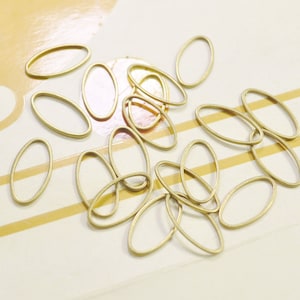 Könnte beinhalten: Ein Haufen ovaler Sprungringe in Goldfarbe. Die Ringe sind auf einer weißen Oberfläche mit goldenen Streifen verstreut.