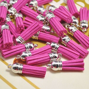 Peut inclure: Un tas de pompons en daim rose avec des embouts en métal argenté. Les pompons mesurent environ 5 cm de long et sont parfaits pour ajouter une touche de fantaisie à n'importe quel projet.