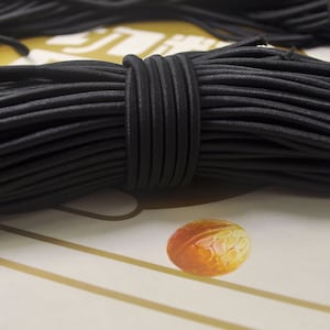 May include: A close-up of a bundle of black elastic cord, tightly wound and secured. The cord appears smooth and slightly shiny. The background is a light color with a small, orange, oval-shaped object.