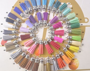 May include: A collection of 50 colorful suede tassels with silver-tone metal caps. The tassels are arranged in a circular pattern, showcasing a wide range of colors, including pinks, blues, greens, yellows, and browns. Each tassel is approximately 2 inches long.