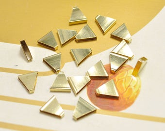 May include: A collection of gold-colored metal triangle shapes, some with a slightly textured surface. The triangles are scattered on a light brown surface.