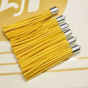 以下が含まれることがあります： 銀色の金属製のキャップが付いた黄色のスエードタッセルが6つ。タッセルは一列に並んでおり、キャップは視聴者の方を向いています。