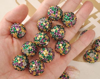 May include: A selection of glittering, spherical beads. Each bead is adorned with tiny, colourful rhinestones in green, purple, and gold. The beads are held in a hand, highlighting their intricate details and vibrant colours.
