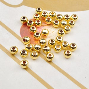 May include: A group of 30 gold-coloured round beads. The beads are smooth and shiny, and they are scattered on a white surface.