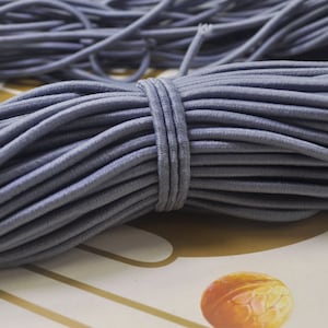 May include: A close-up of a large spool of gray elastic cord. The cord is tightly wound and has a smooth, matte finish.