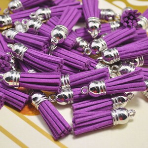 Könnte beinhalten: Eine Gruppe von violetten Samtquasten mit silbernen Metallkappen. Die Quasten sind in einem Stapel angeordnet, wobei sich einige überlappen.