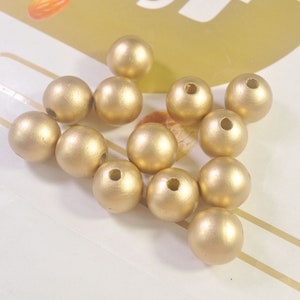 May include: A group of 12 gold wooden beads. The beads are round and have a smooth, matte finish. They are perfect for crafting jewelry or other projects.