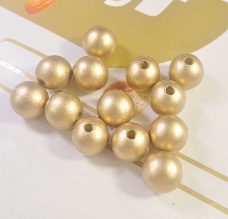 May include: A group of 12 gold wooden beads. The beads are round and have a smooth, matte finish. They are perfect for crafting jewelry or other projects.