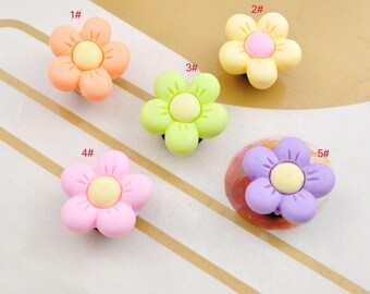 May include: Five colorful flower-shaped charms with yellow centers. The charms are in shades of orange, yellow, green, pink, and purple.