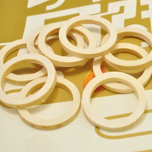 May include: A group of 10 off-white, round, plastic rings. The rings are stacked and overlapping.