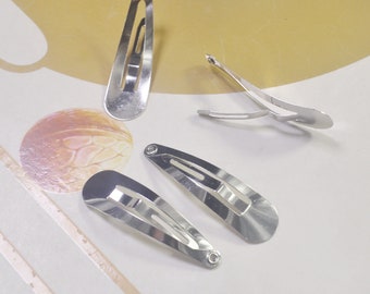May include: Four silver metal hair clips. The clips are oval shaped with a small hole at the top. The clips are designed to hold hair in place.