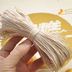 Könnte beinhalten: Eine Spule mit naturfarbenem Garn aus Papier, das in einer Hand gehalten wird. Das Garn ist fest gewickelt und wirkt sehr robust.