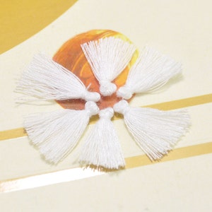 May include: Five white cotton tassels arranged in a star shape on a white and gold surface.