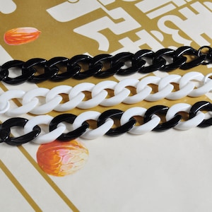May include: Three black and white plastic chain straps with metal clasps. The chains are linked together in a repeating pattern.