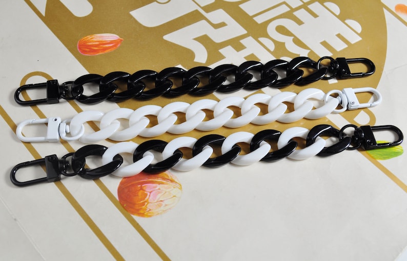 May include: Three black and white plastic chain straps with metal clasps. The chains are linked together in a repeating pattern.