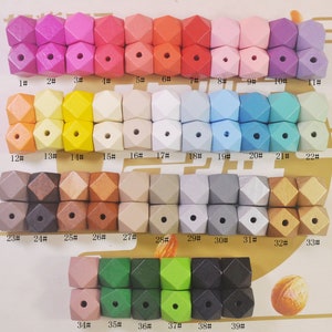 Może przedstawiać: Zestaw 39 drewnianych koralików w różnych kolorach i wykończeniach. Korale mają kształt 12-ściennej kostki do gry i mają otwór w środku. Korale są ponumerowane od 1 do 39.