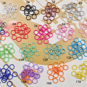 Può includere: Assortimento di 17 diverse dimensioni di anelli aperti in vari colori, tra cui bianco, nero, marrone, grigio, rosso, rosa, blu, verde, giallo e viola. Ogni dimensione è etichettata con un numero da 1 a 17.