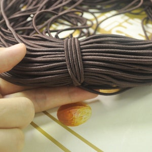 May include: A close-up of a large spool of brown elastic cord. The cord is tightly wound and appears to be made of a soft, stretchy material.